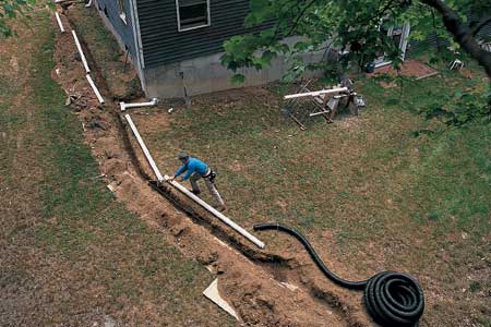 Exterior drain piping being installed in a narrow yard beside a home