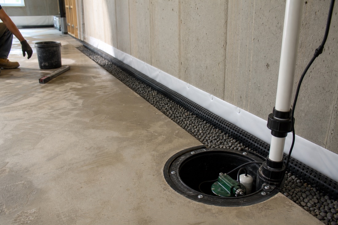 Interior French drain channel feeding an open sump pump basin along a basement wall